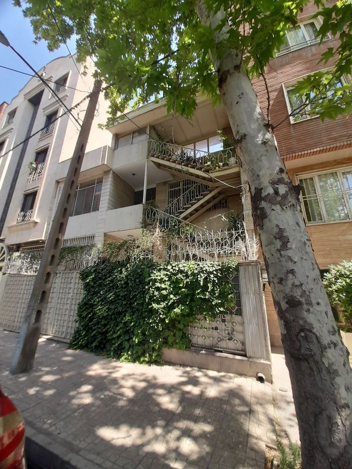 پلکان و بالکن الحاقی با گیاهان، روی نمای یک ساختمان چندطبقه، از پایین دیده‌شده — An added stair and planted balcony on a multi-storey facade, seen from below
